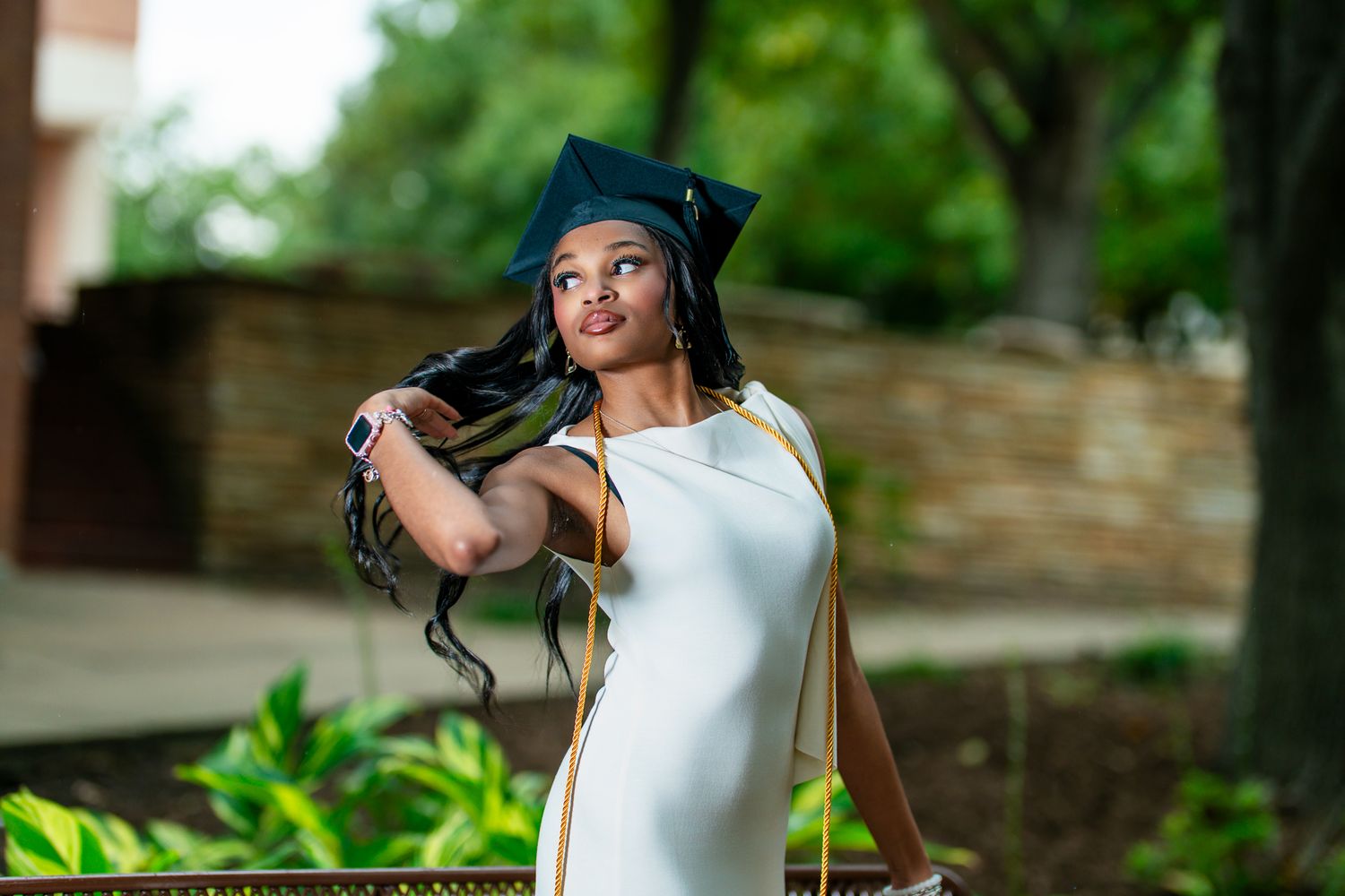 Portrait of someone in a white dress and graduation cap posing outdoors near greenery. Powerrpackmedia Houston Texas