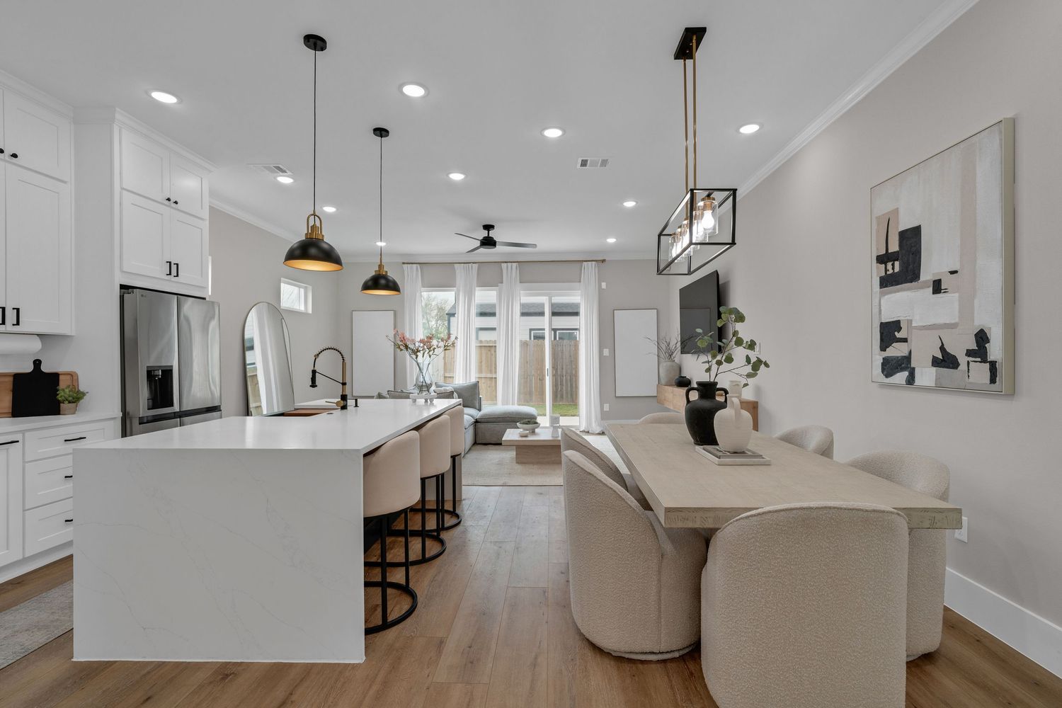 Modern open-concept kitchen with white cabinets, large island, pendant lights, and seamless flow into bright living and dining areas.