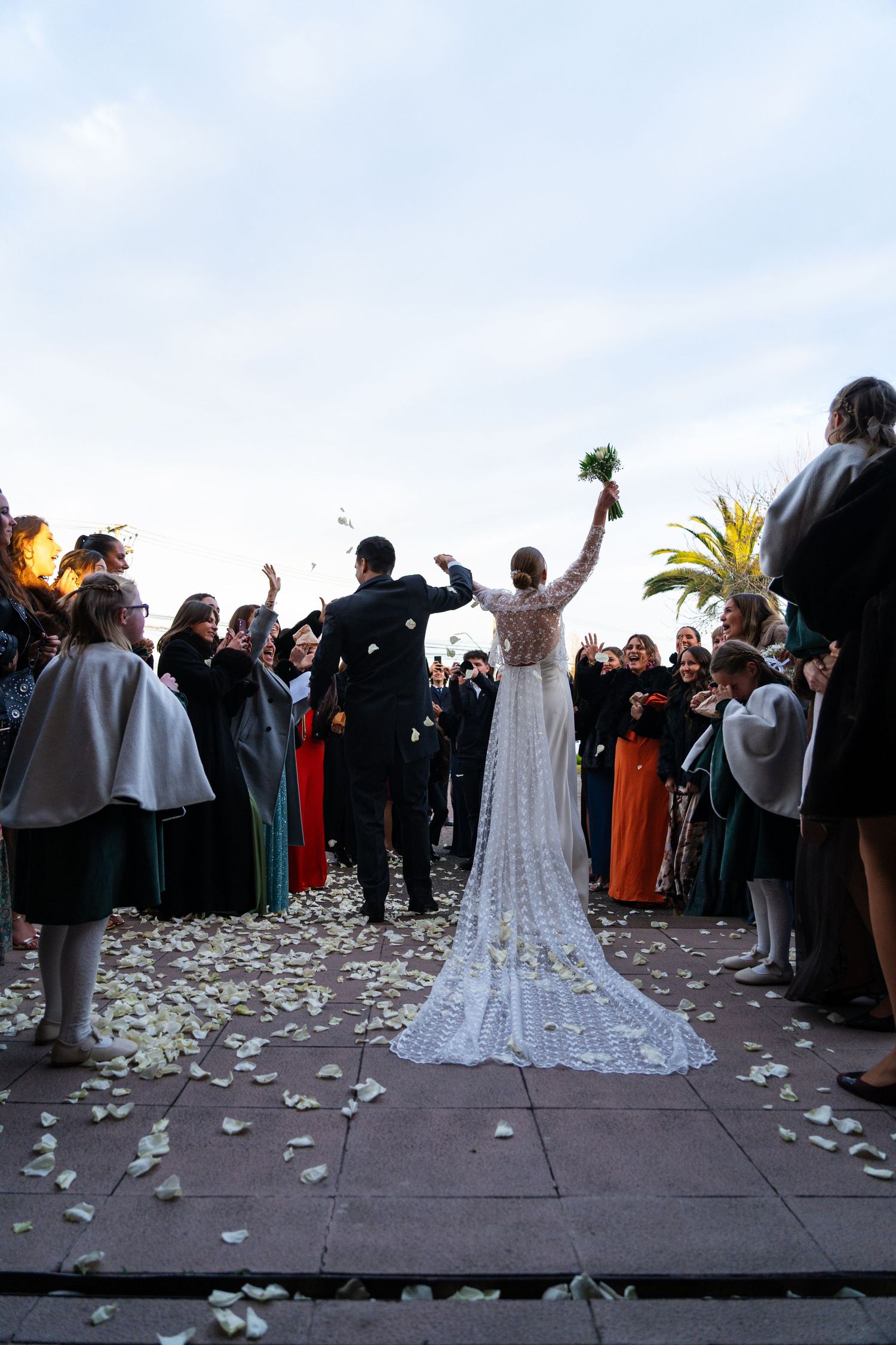 Outdoor wedding celebration with guests throwing petals as bride stands in long white dress.