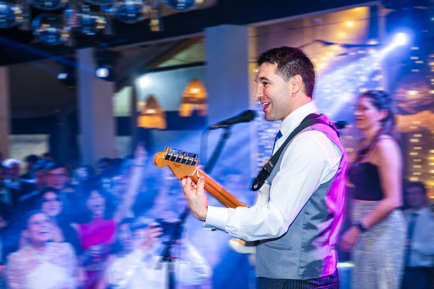 Musician performing with a guitar under blue stage lighting at a wedding reception.