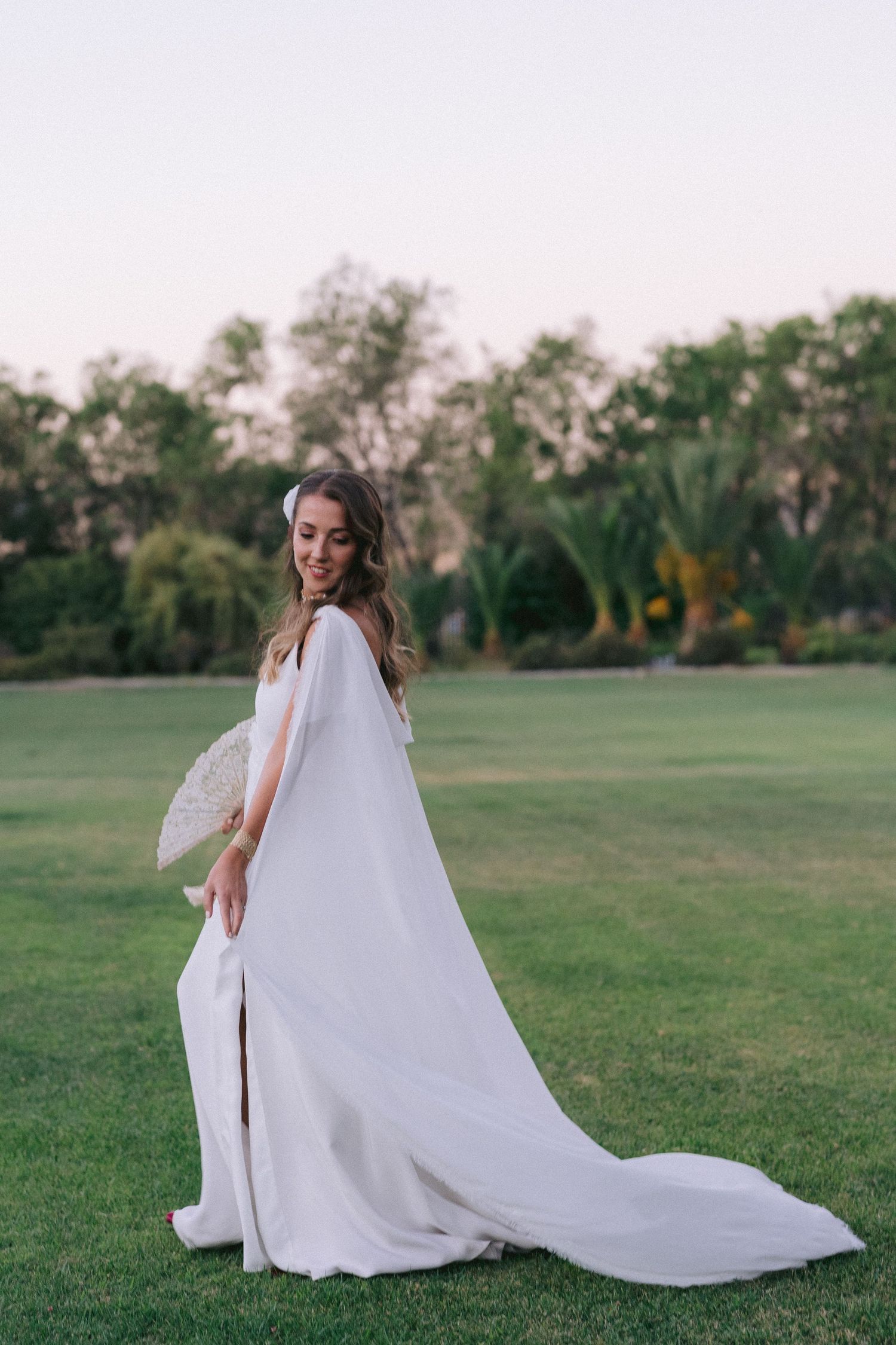 Person in flowing white wedding dress twirling in an open green field.