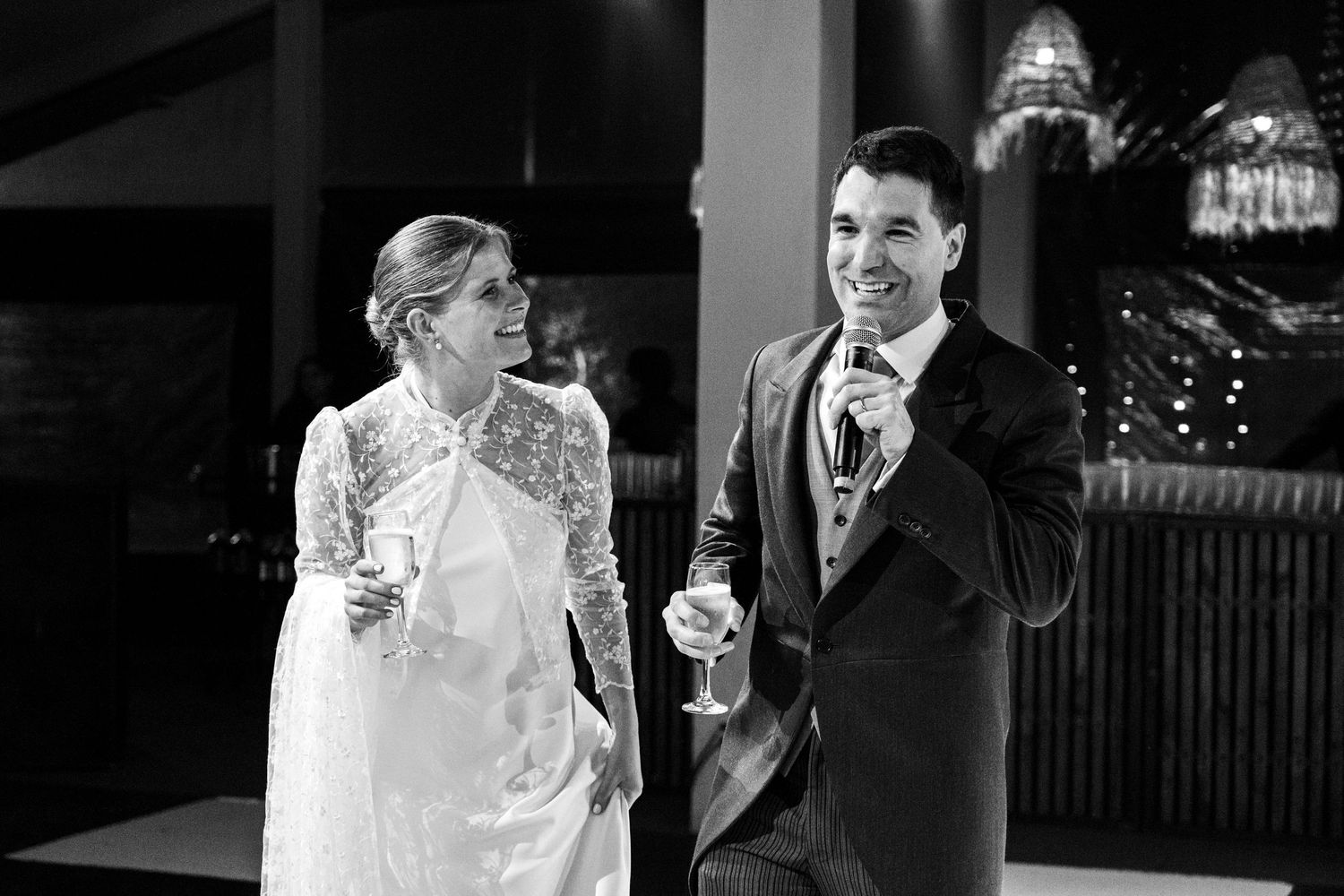 A black and white photo of a couple sharing champagne and laughter during their wedding reception.