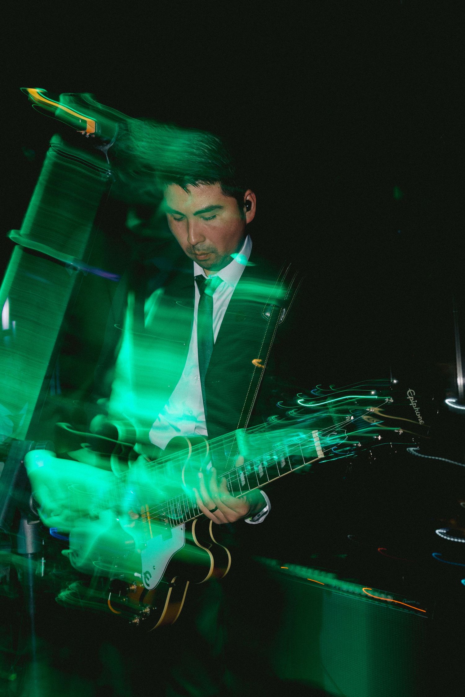 A guitarist performs under dramatic green stage lighting creating a moody atmospheric effect.