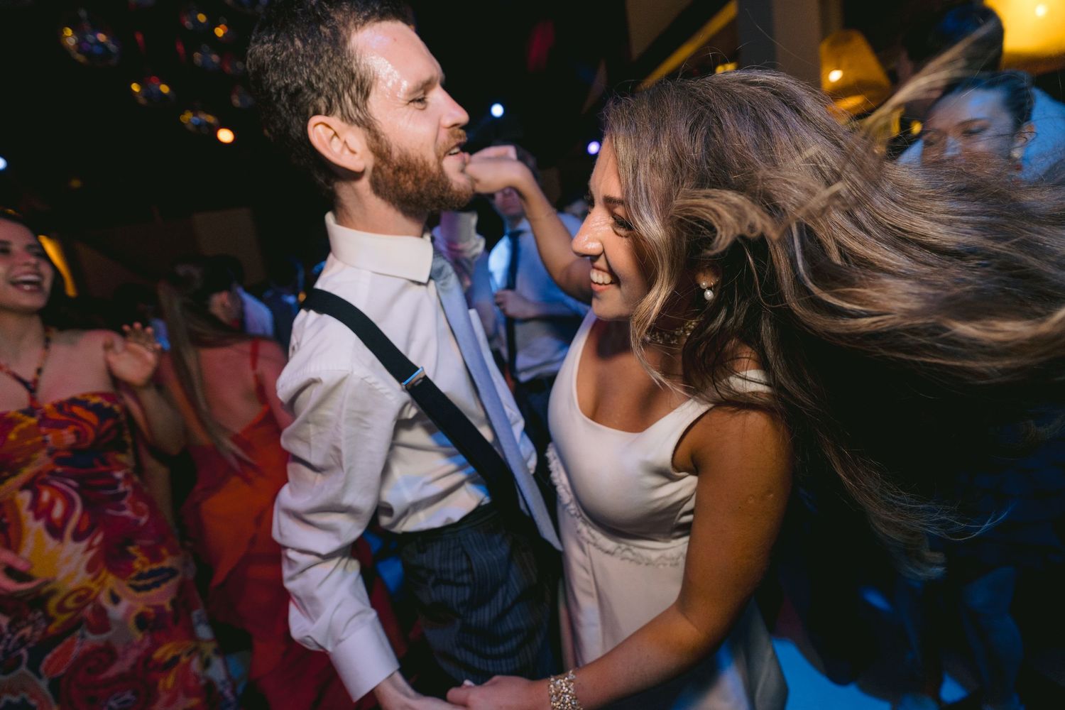 Wedding guests dancing and celebrating in formal attire under ambient lighting.