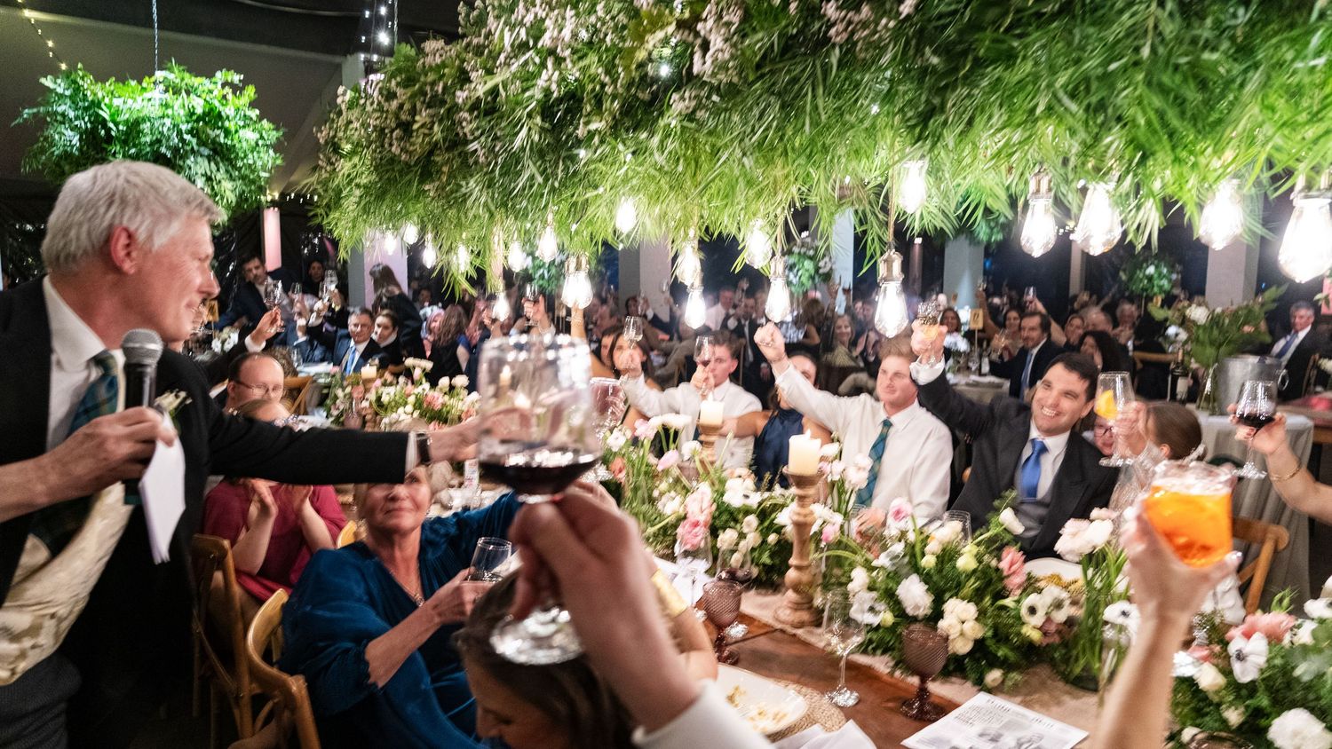 Outdoor wedding reception venue decorated with hanging greenery and floral arrangements.