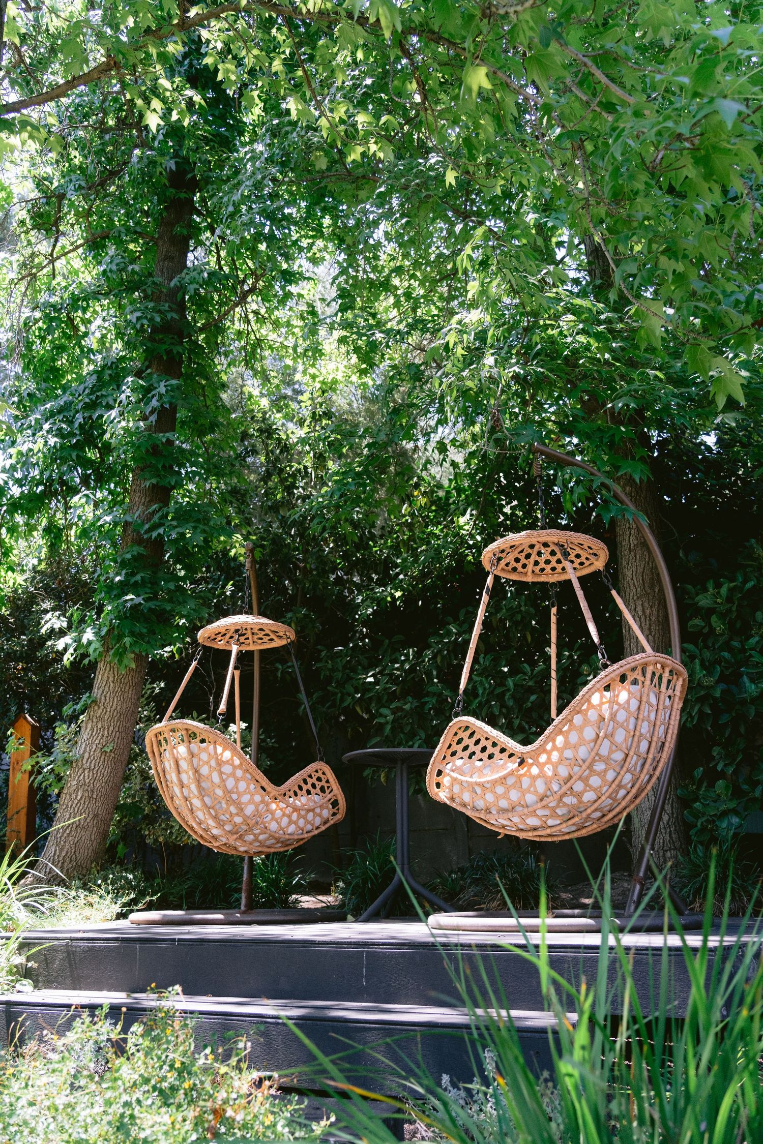Row of hanging wicker egg chairs in a lush garden setting.