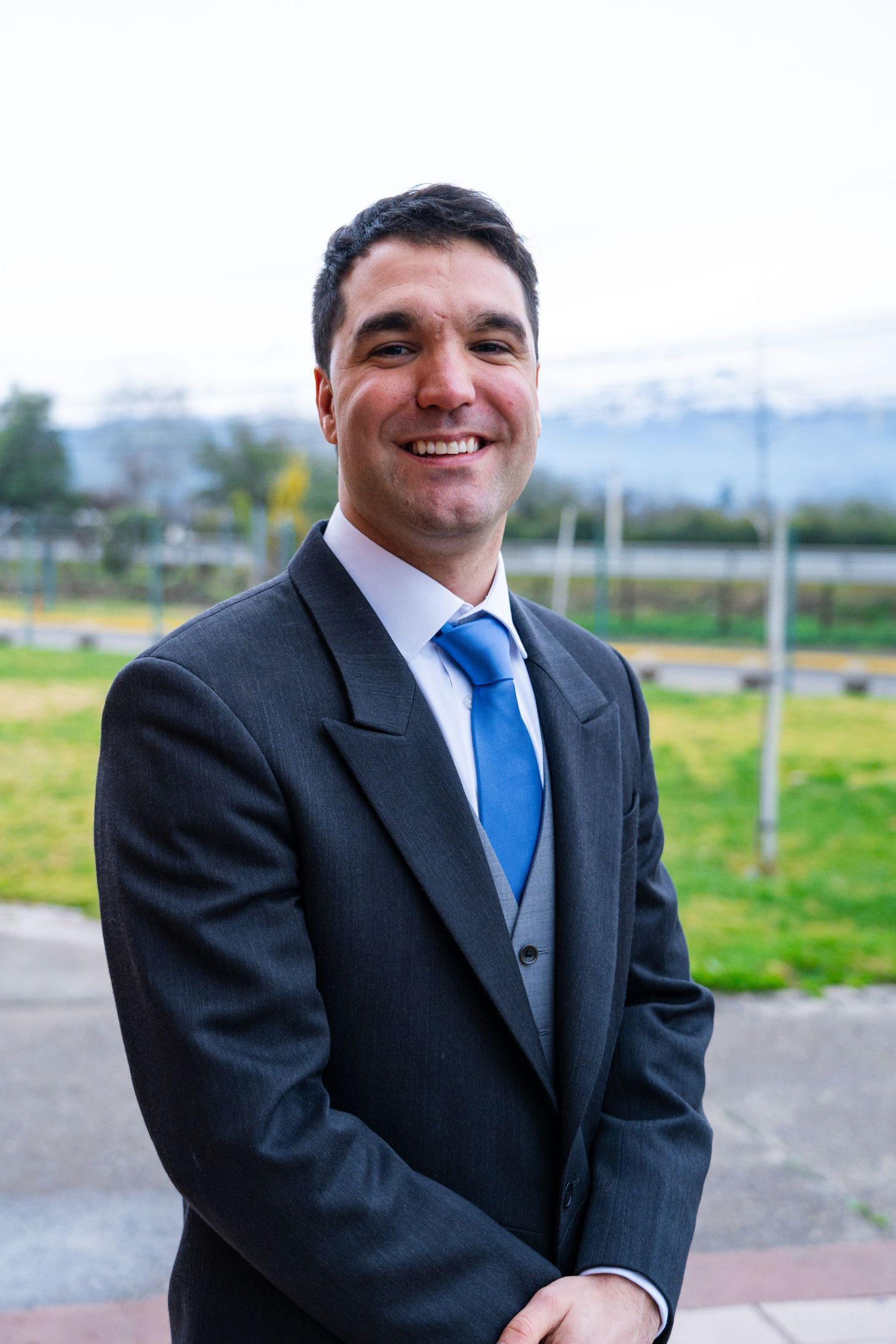 Groom in dark suit with blue tie poses outdoors on wedding day.