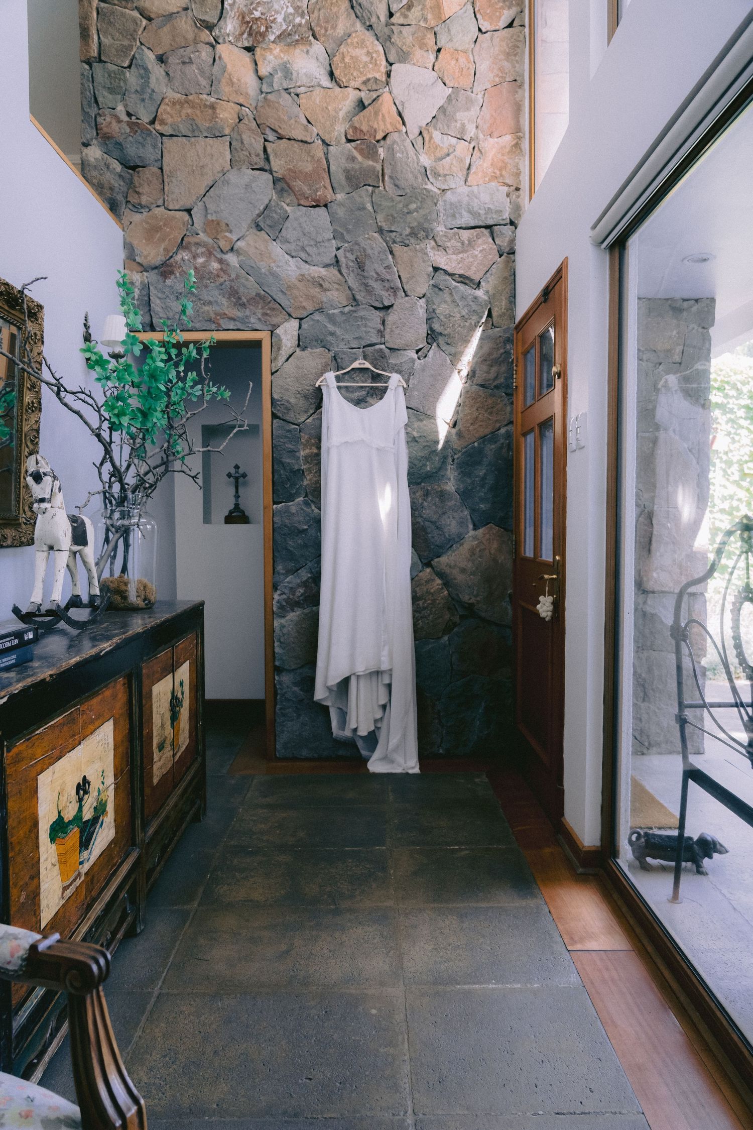 Interior hallway with stone walls displaying white wedding dress on hanger.