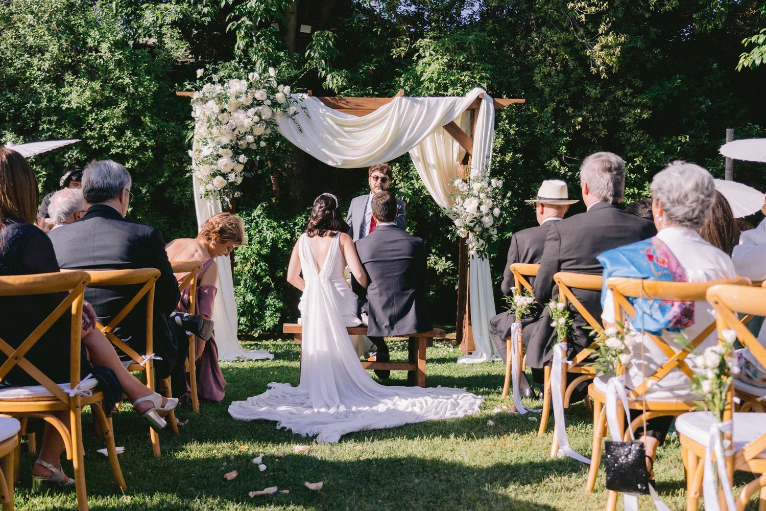 Outdoor wedding reception setup with wooden chairs and decorative fabric canopy.