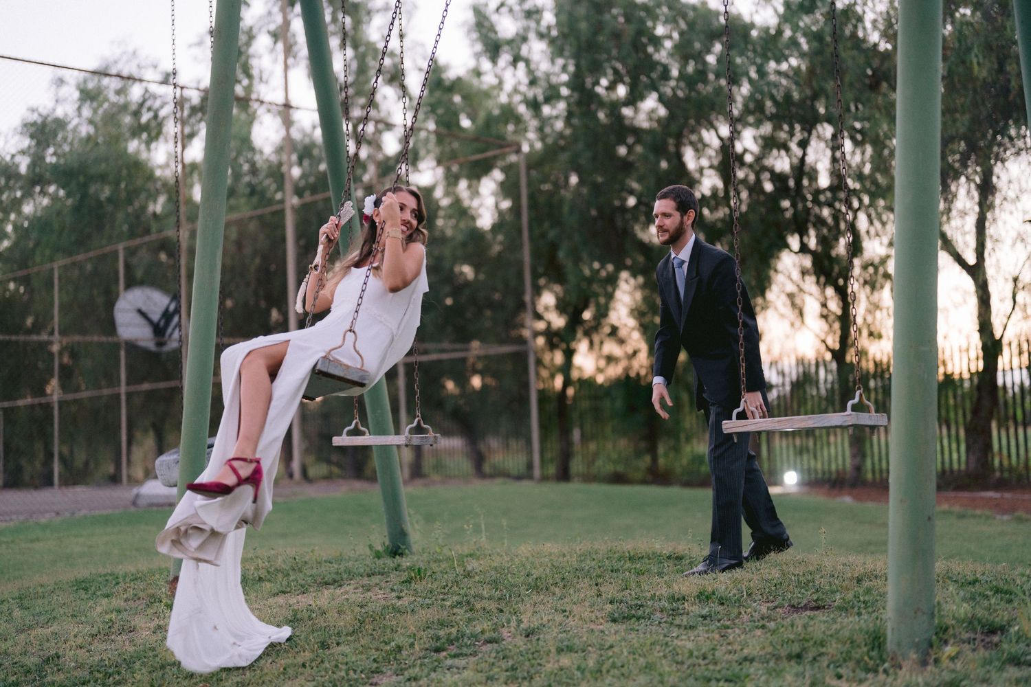 Couple enjoying playful moments in a garden setting with tall trees.