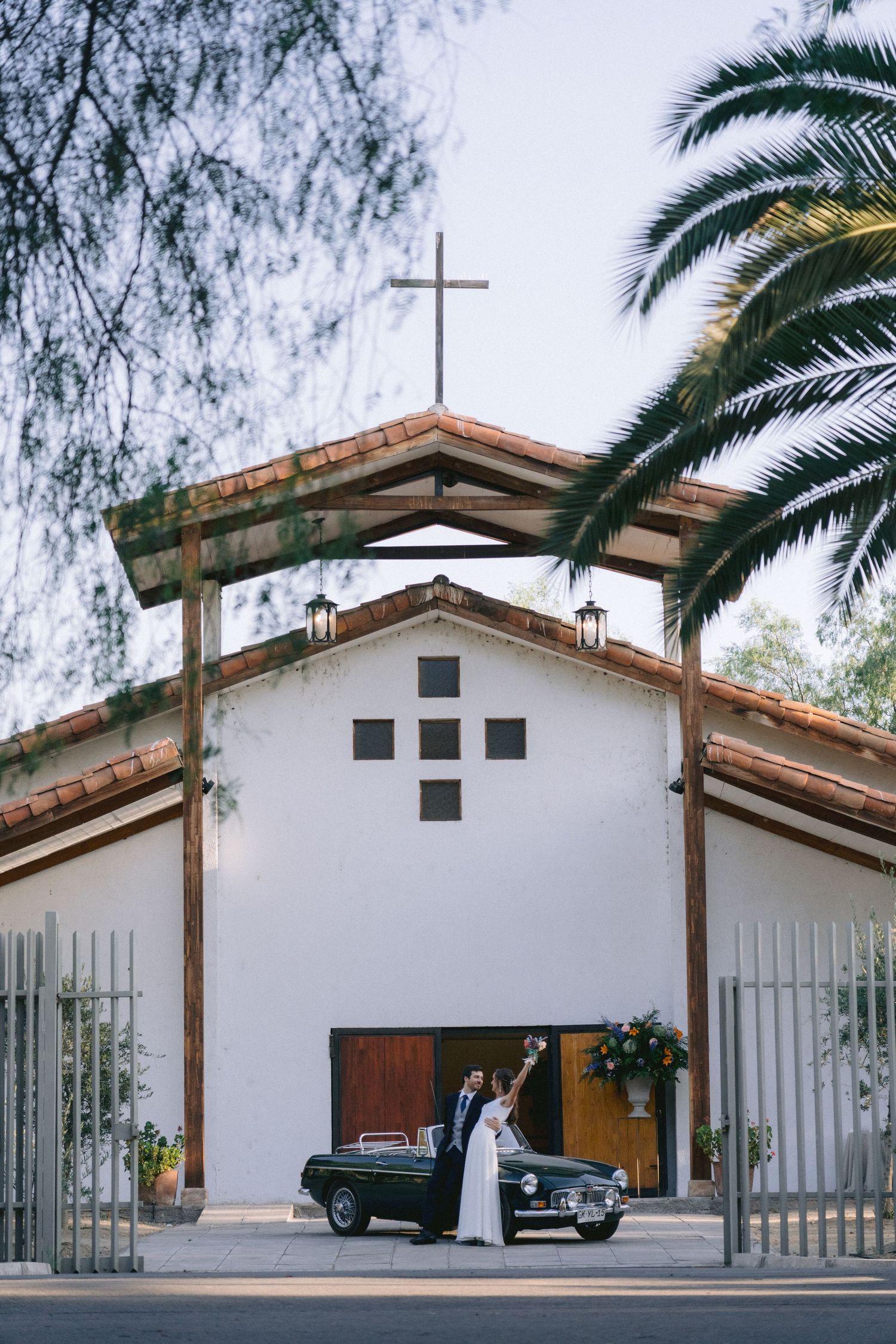 White mission-style church exterior with palm trees and classic car parked outside.