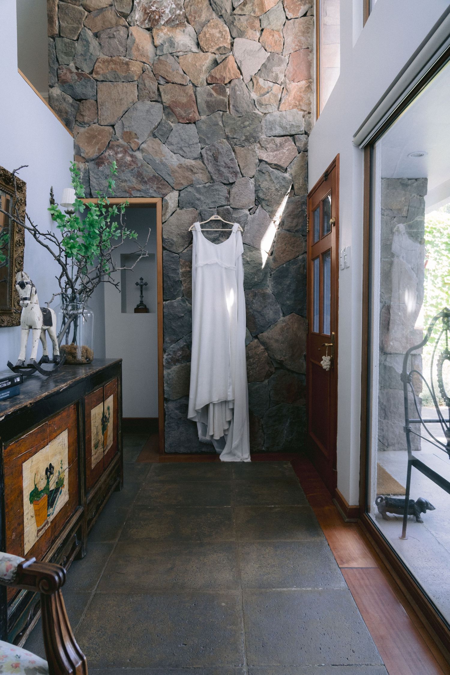 Interior hallway with stone wall and wooden accents displaying a white dress on a hanger.