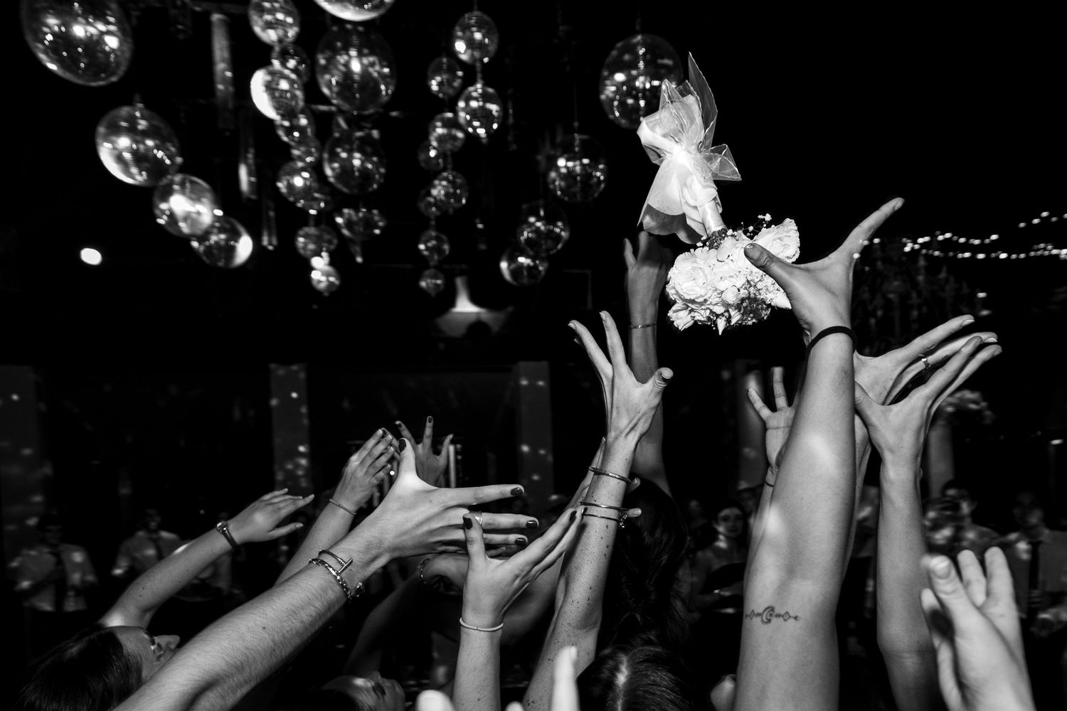 Silhouettes of party guests with raised arms dancing under disco balls and string lights.