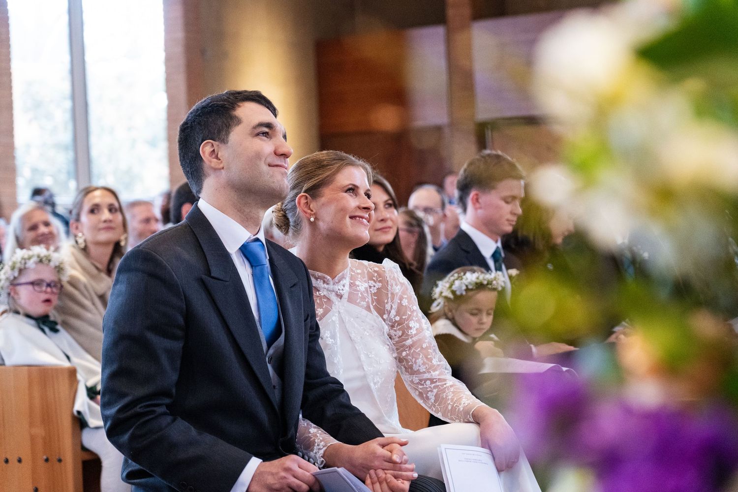 Couple seated during church wedding ceremony with natural light streaming through.