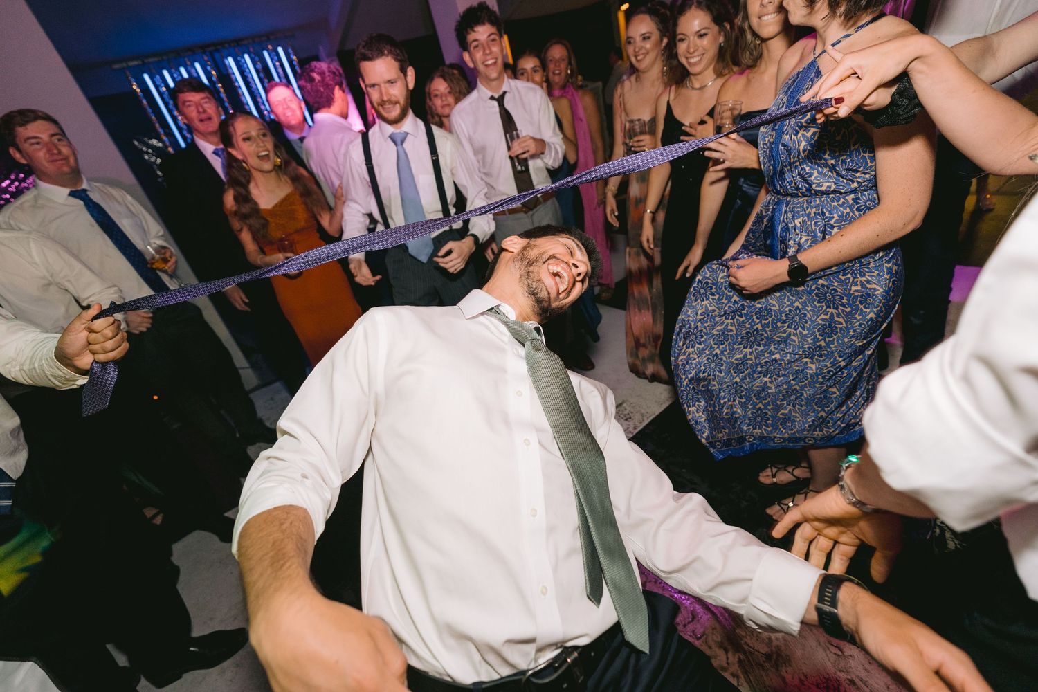 Large group of wedding guests dancing together in formal attire at an indoor reception.