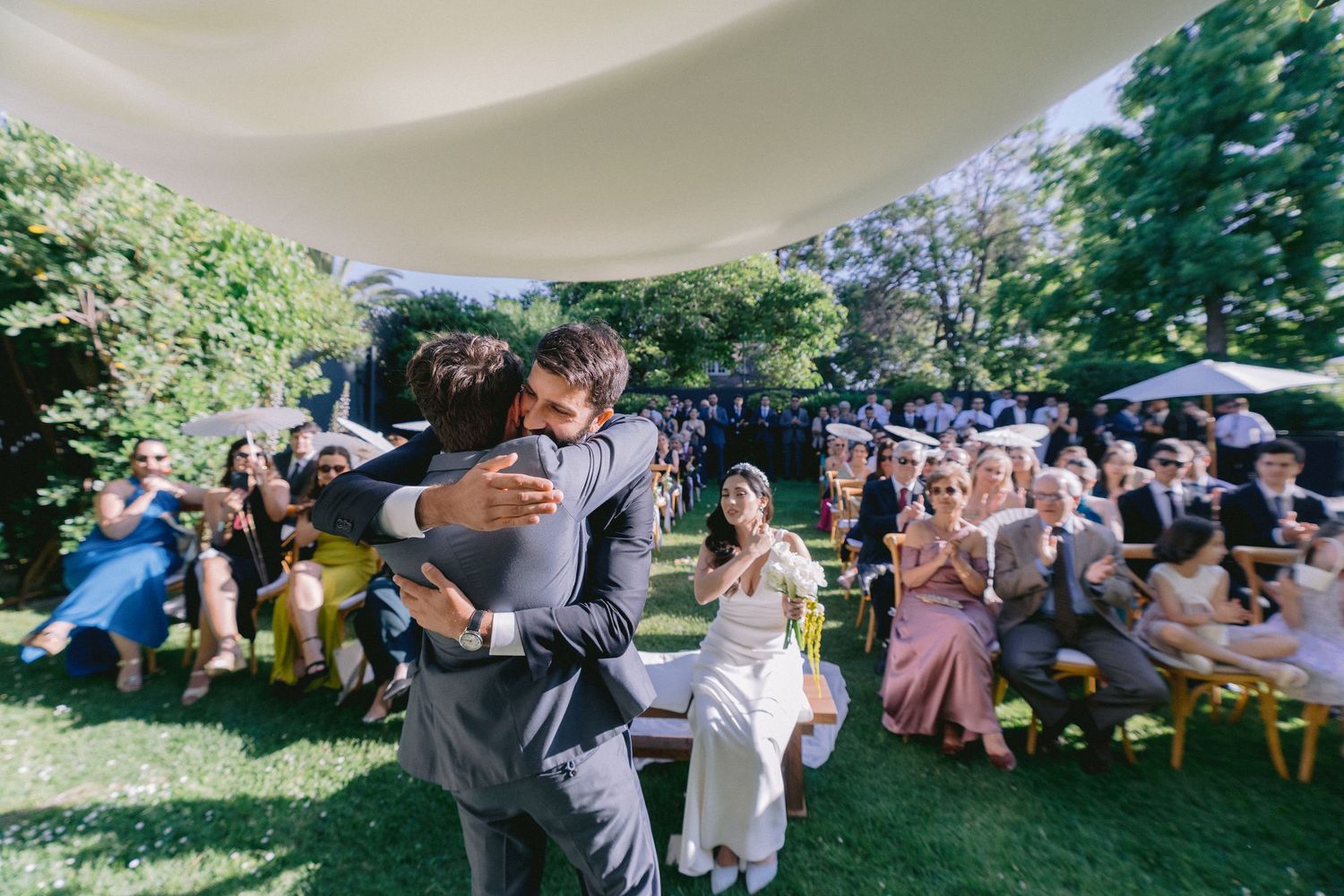 Garden wedding reception with guests seated at tables under natural lighting.
