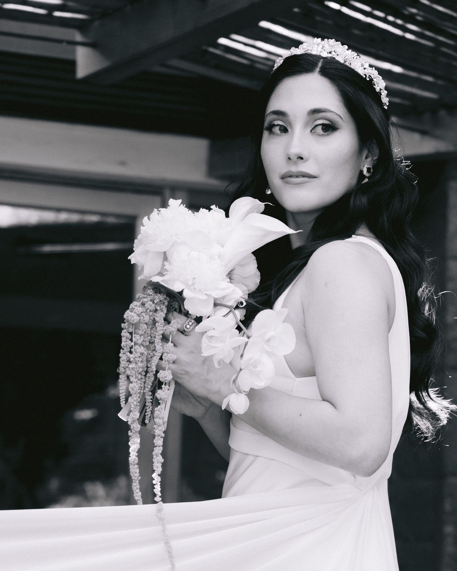 Black and white portrait of bride in white dress holding a bouquet against dark background.