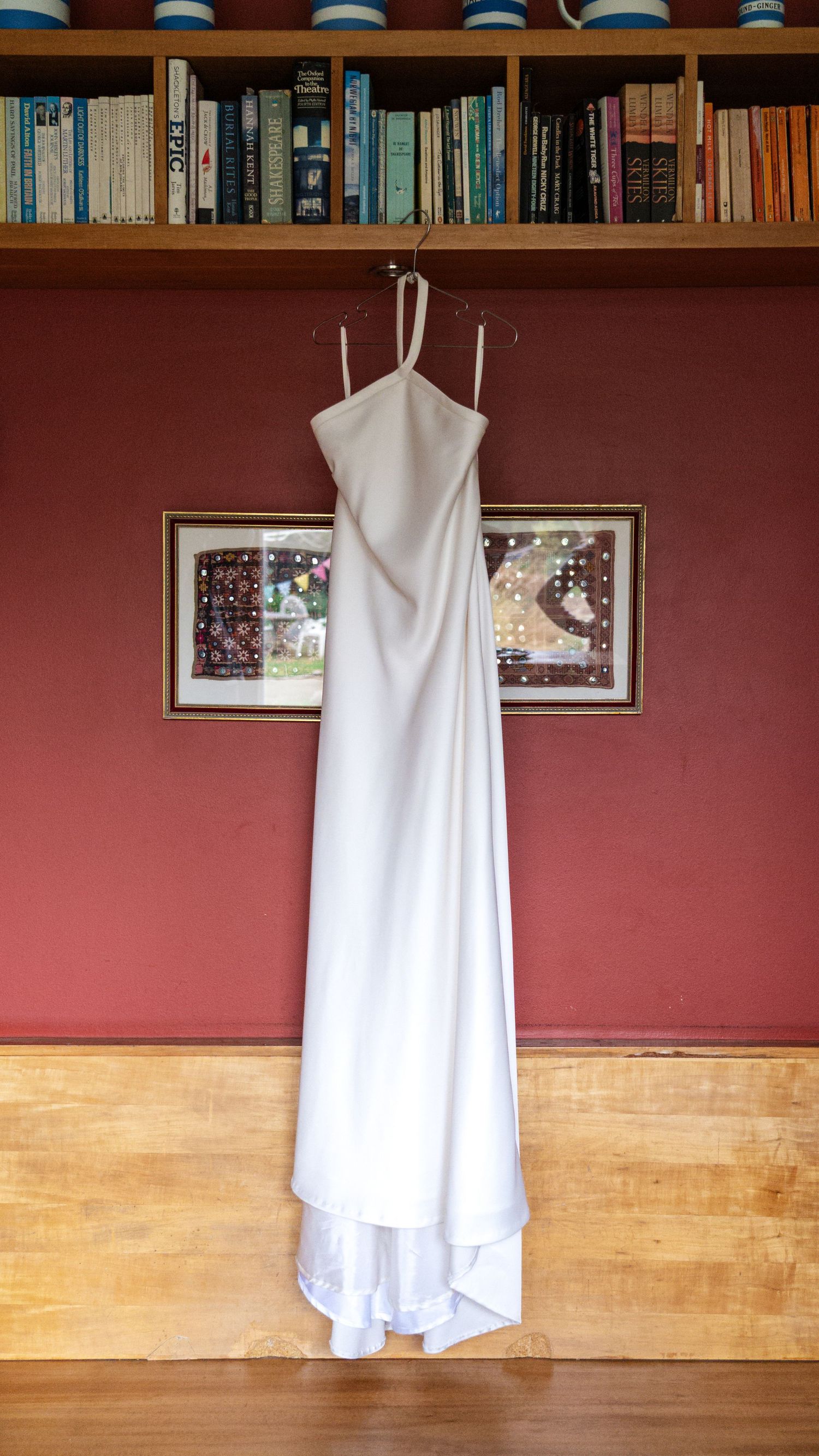 White wedding dress hanging against red wall with bookshelf above.