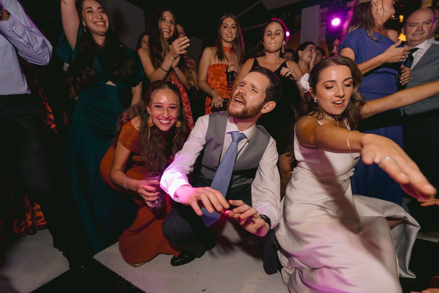 Wedding party guests dancing enthusiastically during an evening reception celebration.