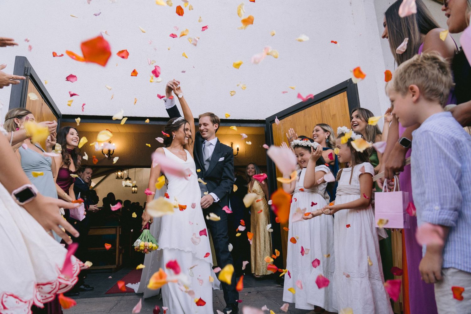 Wedding guests celebrate as rose petals fall during an outdoor reception celebration.