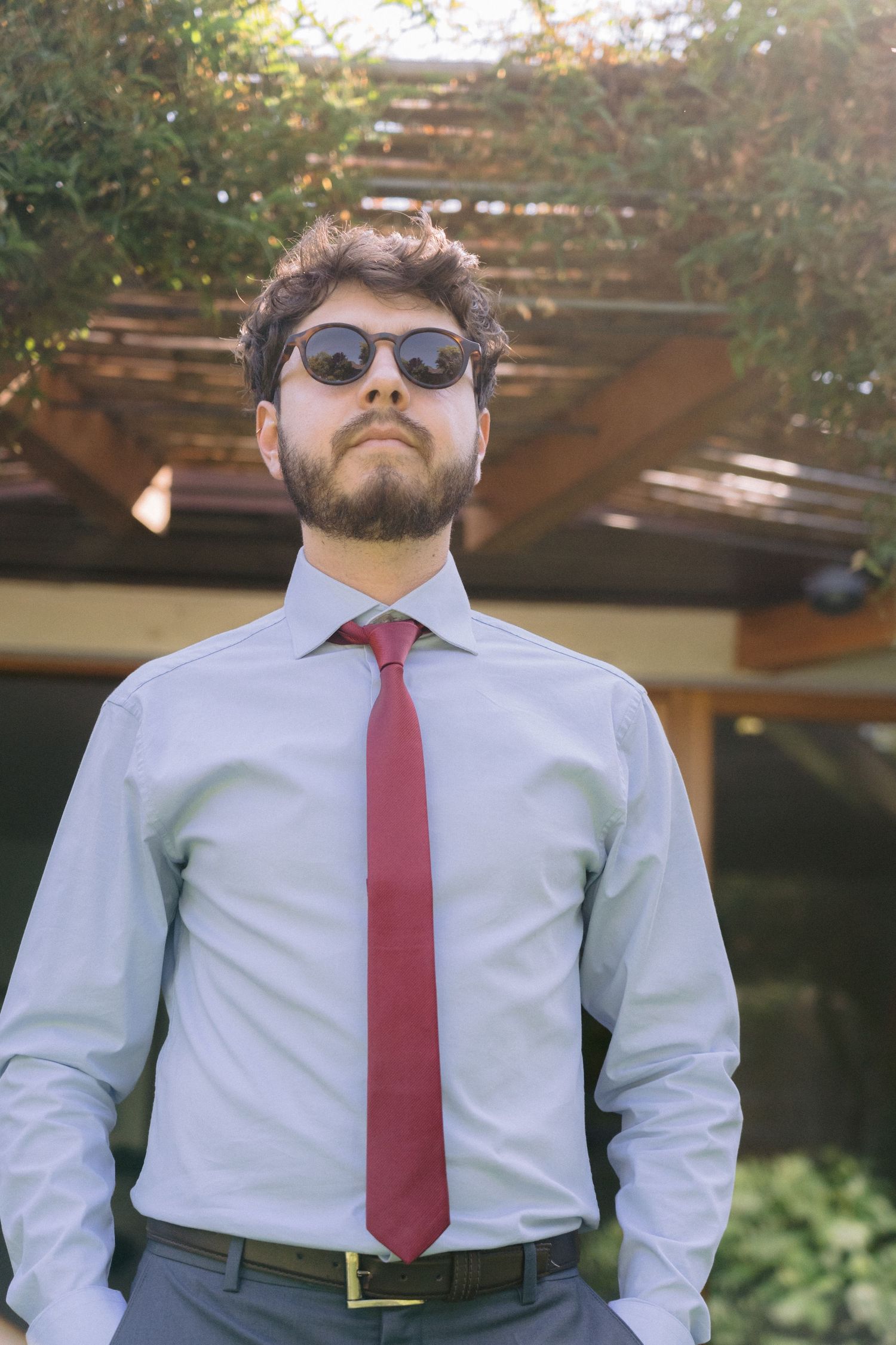 A person in business attire wearing sunglasses posing outdoors.