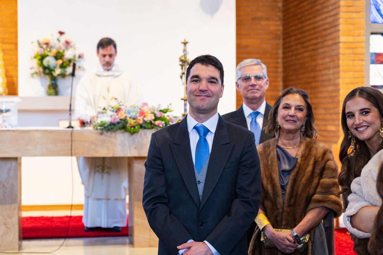 Wedding ceremony in a brick church with floral arrangements on the altar.