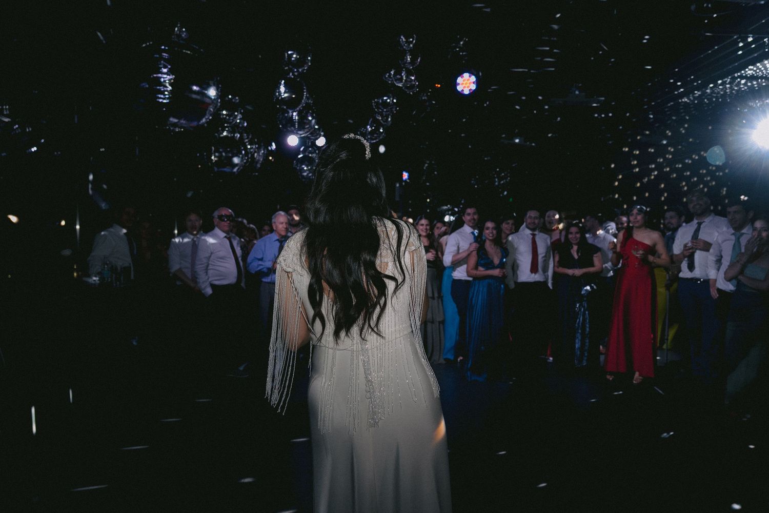 Dark reception venue with silhouettes of guests and twinkling lights in the background.
