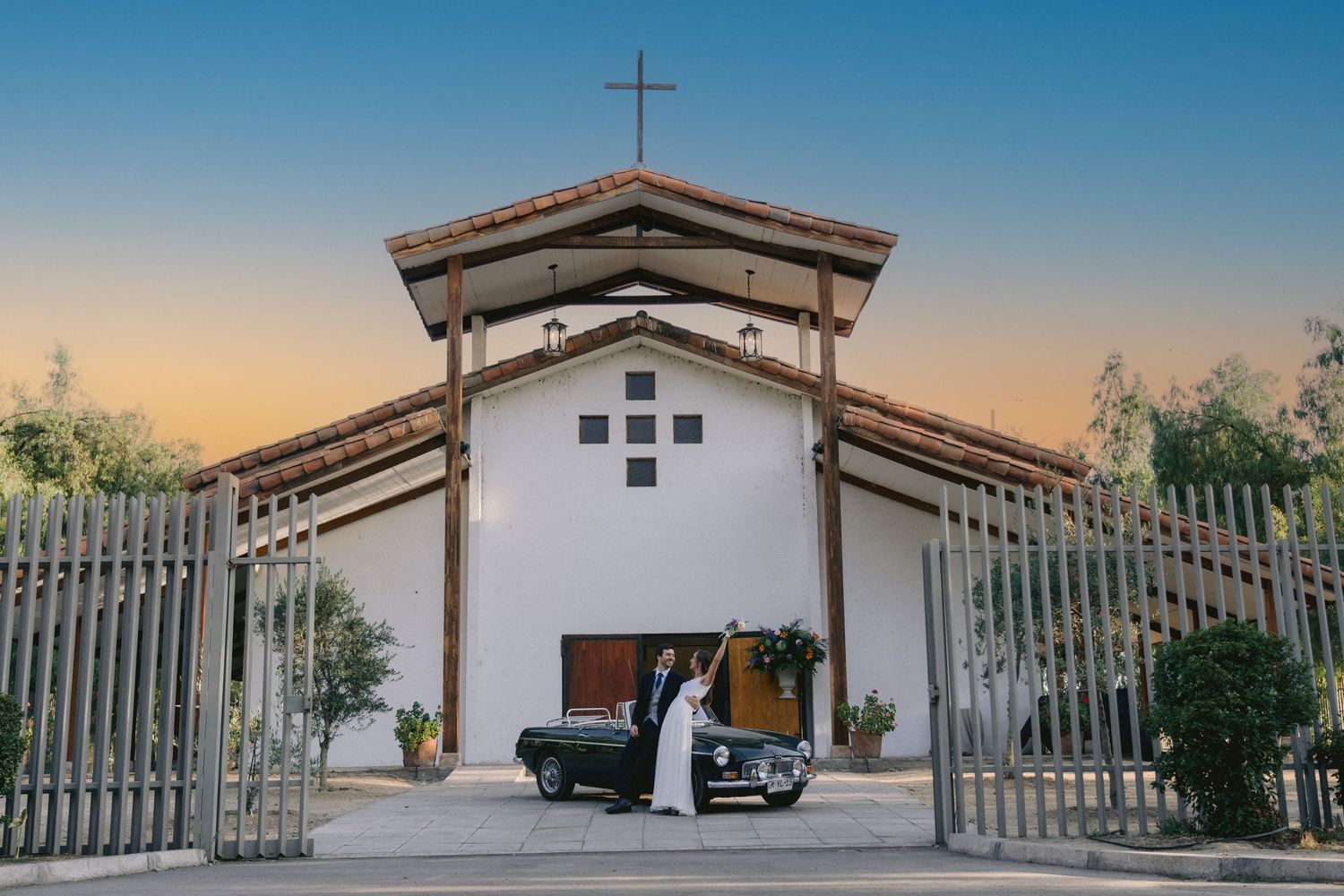 White Spanish mission style church with cross and gates at sunset.