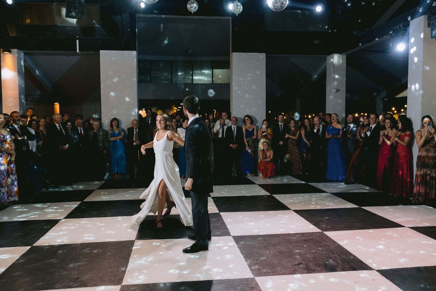 Elegant ballroom with checkered dance floor and guests watching from the sides.