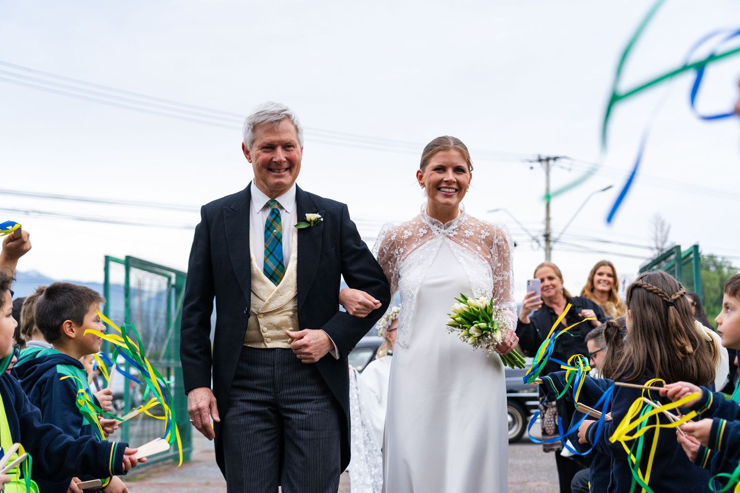 Wedding ceremony processional on a bright day with guests holding colorful ribbons.