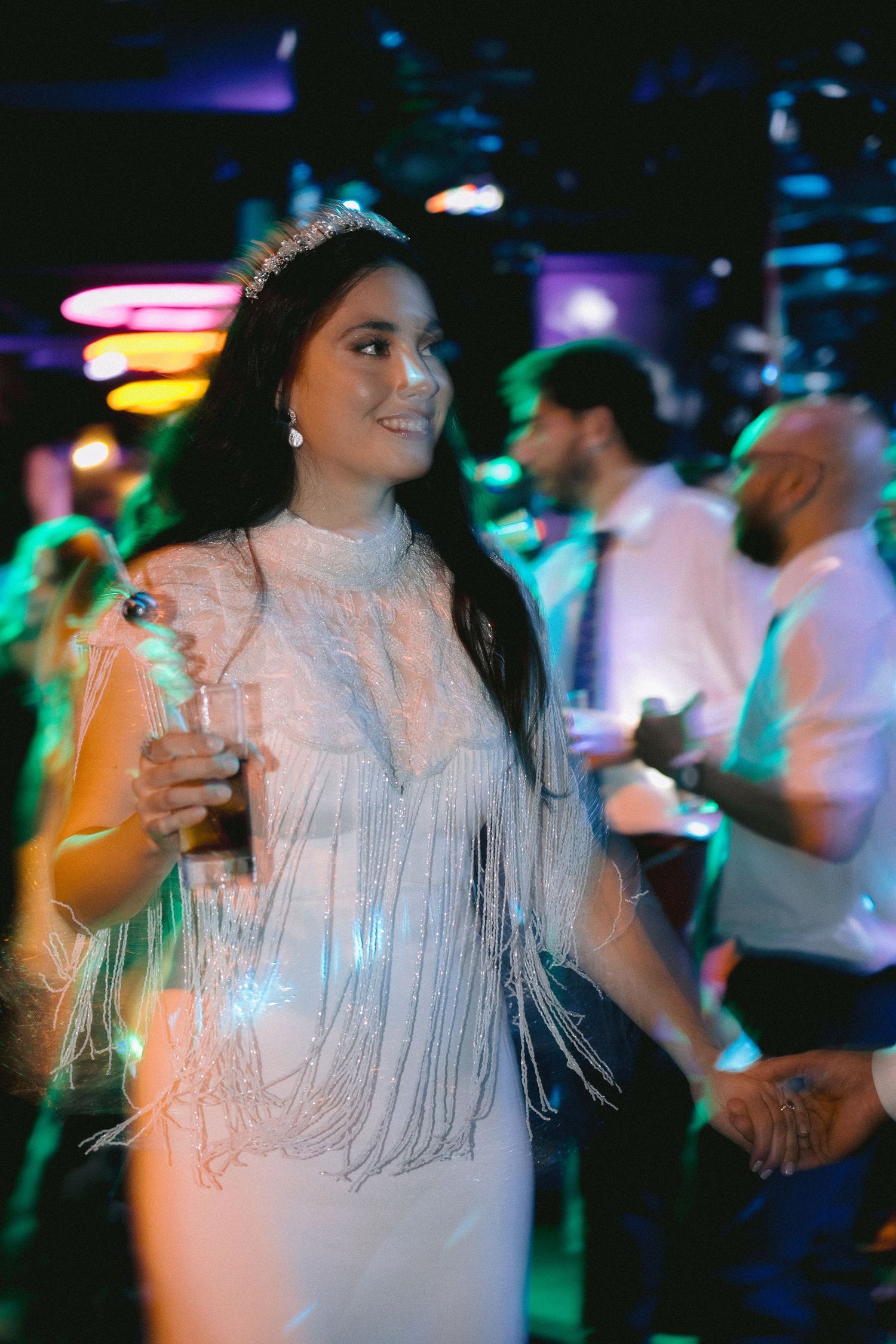 A person in a white fringed dress dances under colorful party lights at a celebration.