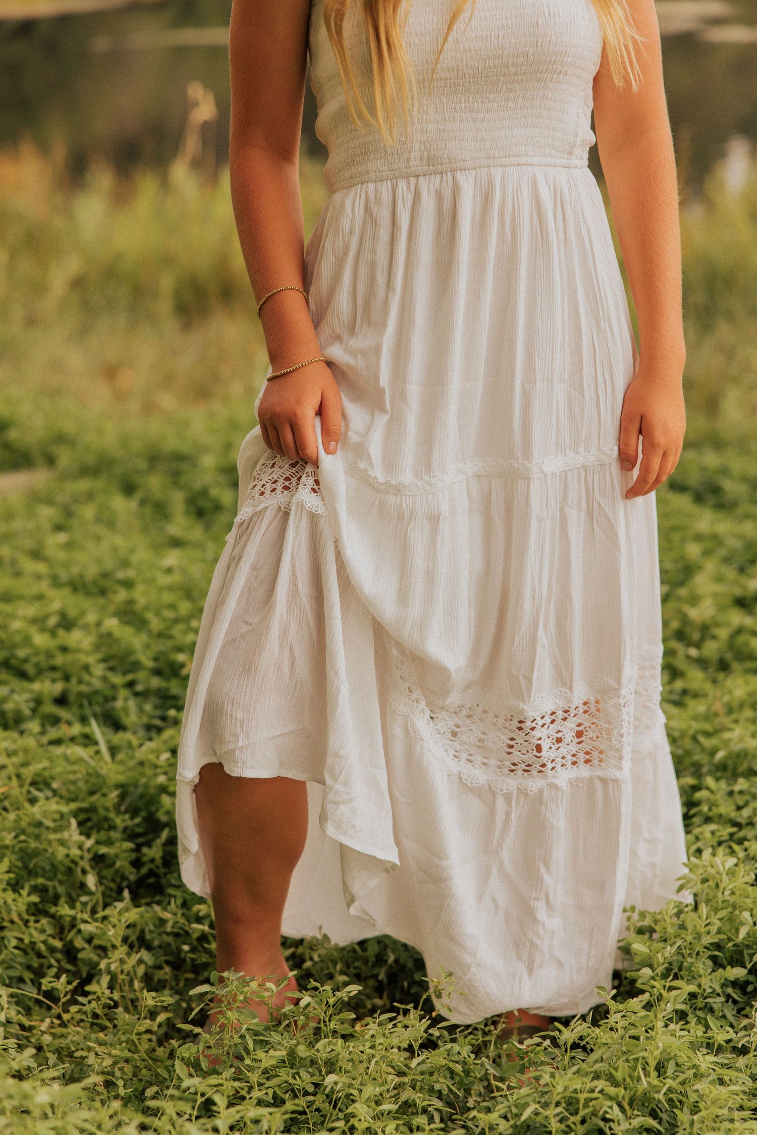Close-up details of a white eyelet lace dress with tiered ruffles against green foliage.