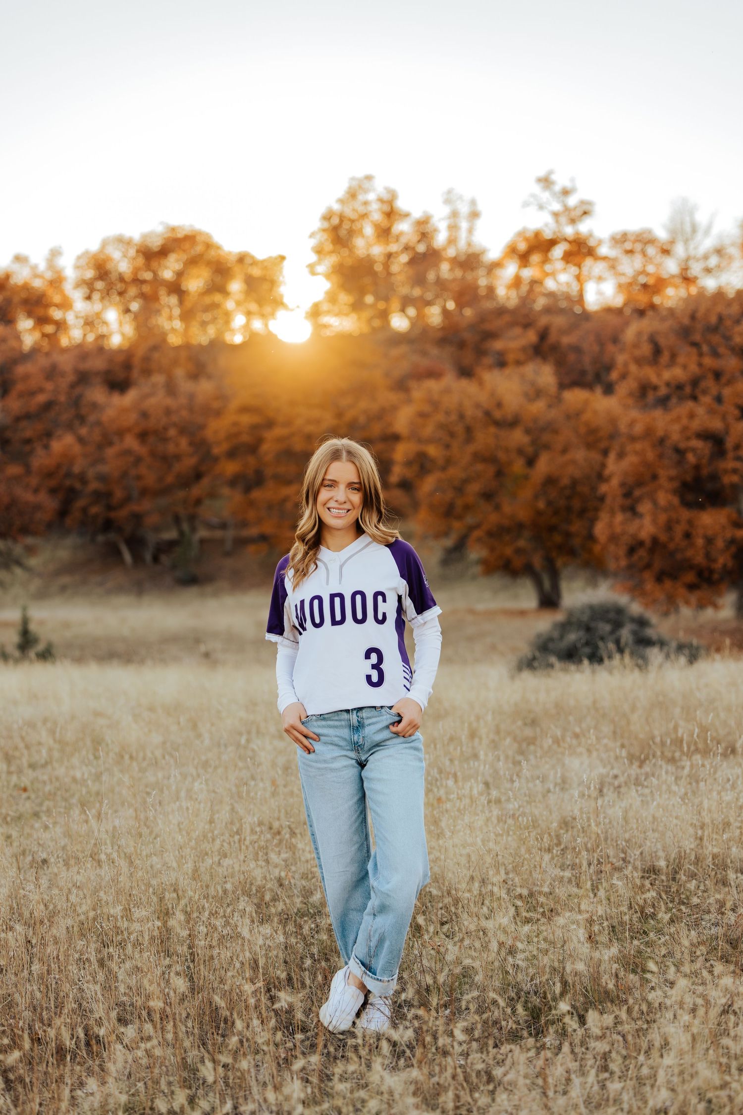 Sports-themed senior photos with jerseys against autumn trees at sunset.