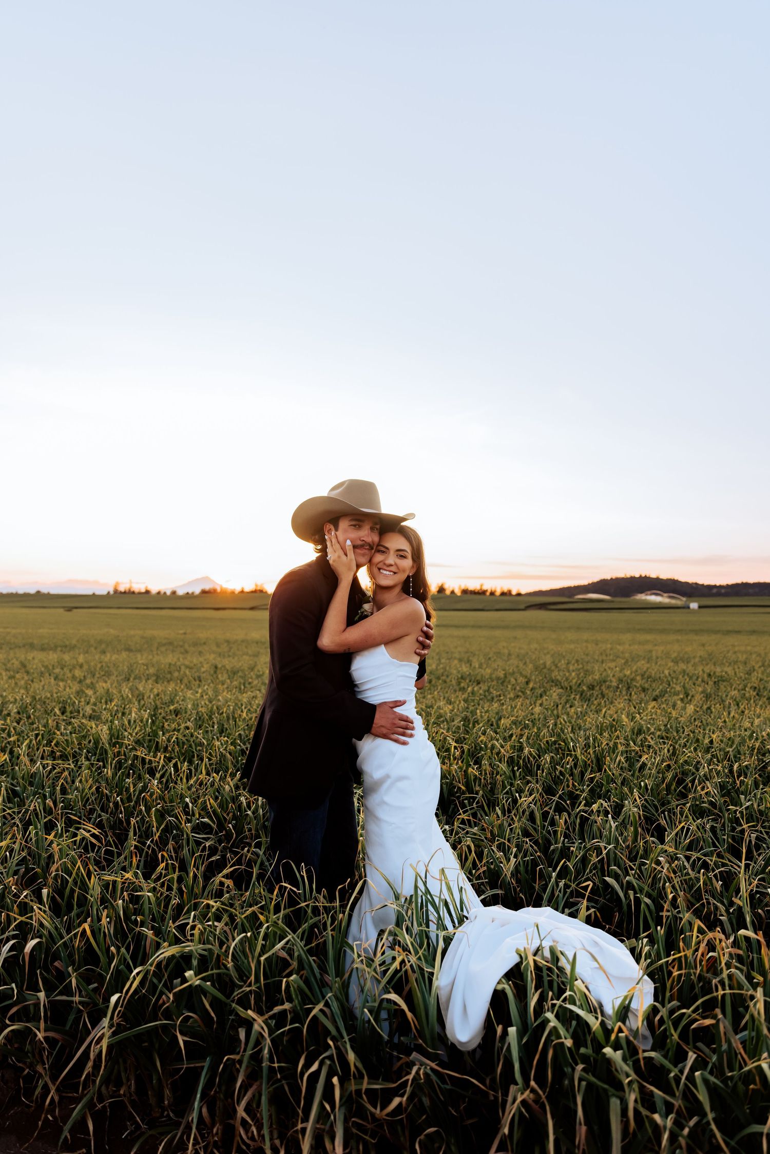 A romantic couple embraces in a cornfield at sunset during their wedding photoshoot.