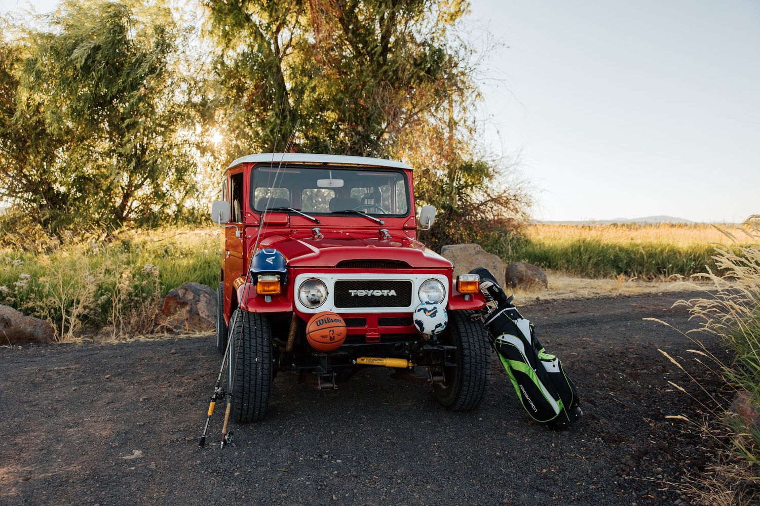 A classic red Toyota Land Cruiser parked among trees during golden hour.
