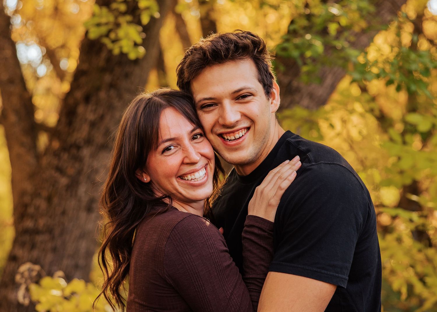 Couple shares joyful laughter while sitting together in a golden autumn forest setting.