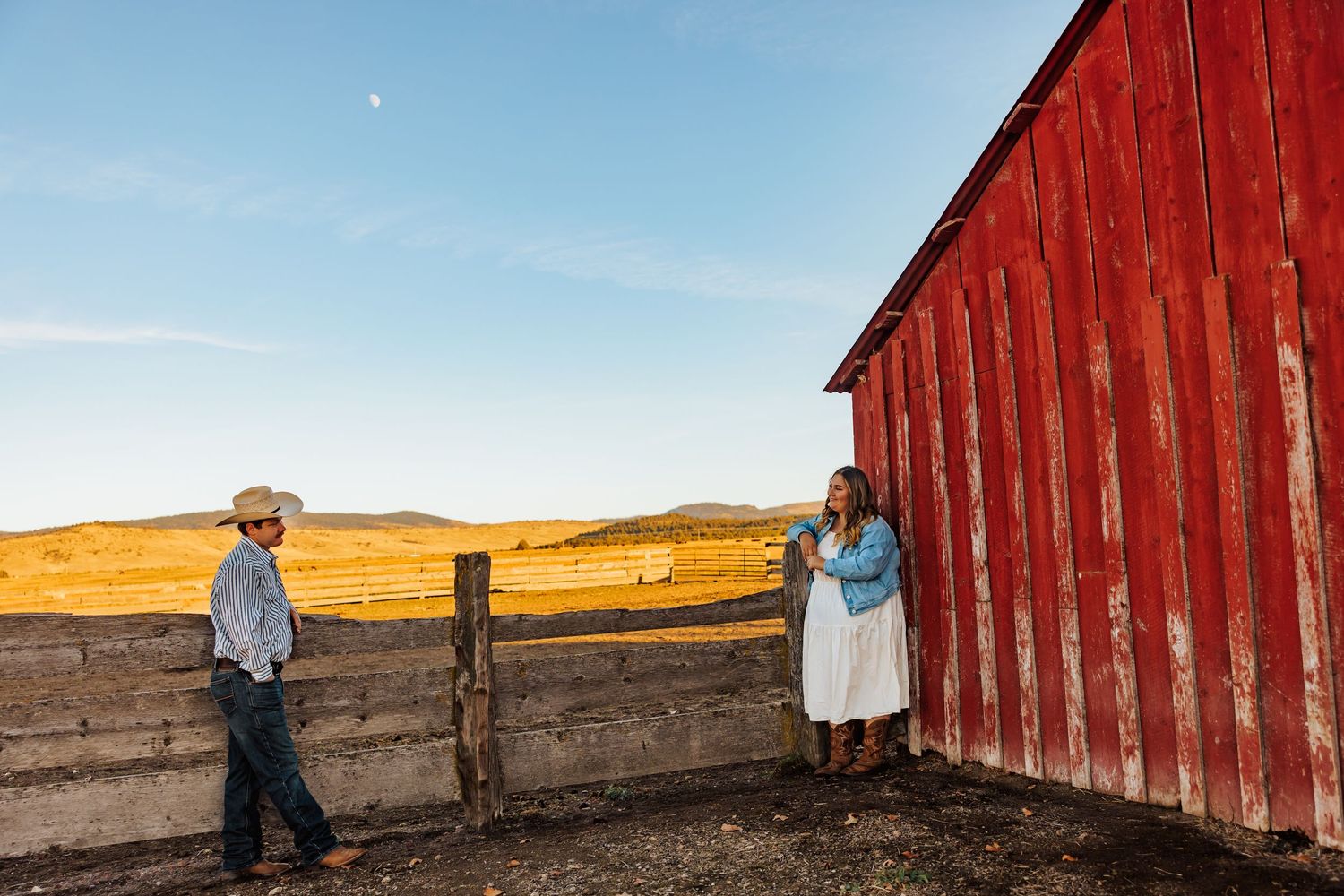A red barn stands against golden hills during a sunset photo session.