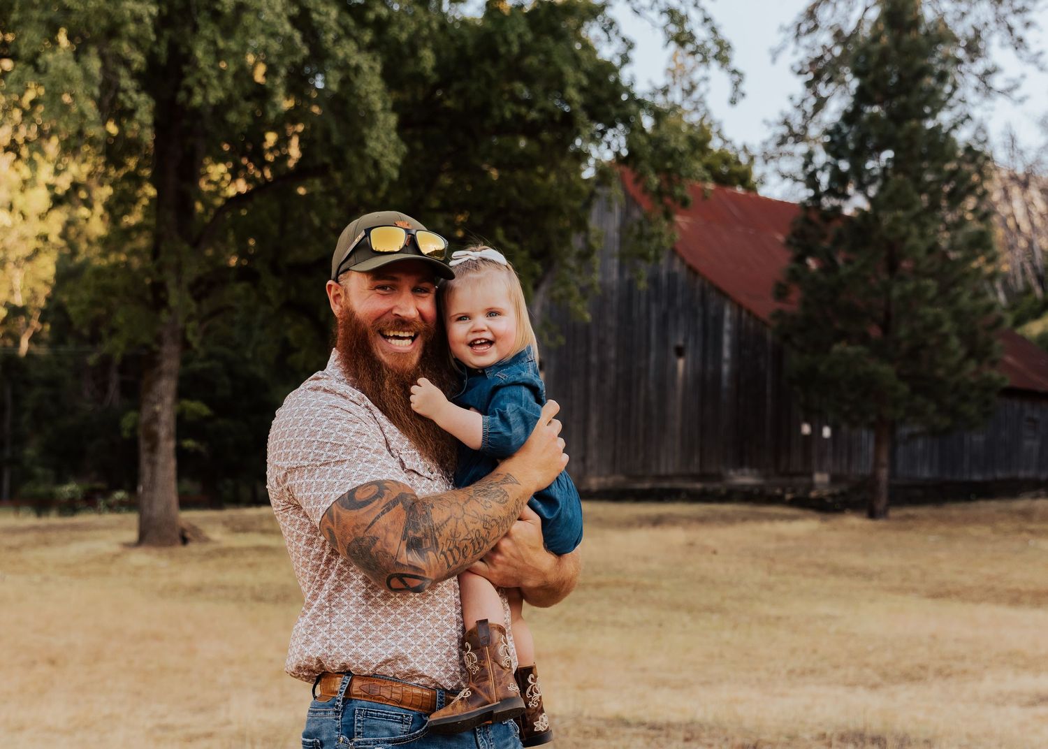A romantic photoshoot in a rustic outdoor setting with a weathered barn and golden field in the background.