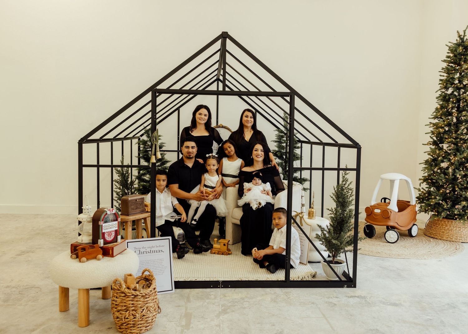 A decorative black metal greenhouse frame displayed against a white wall with holiday decor.