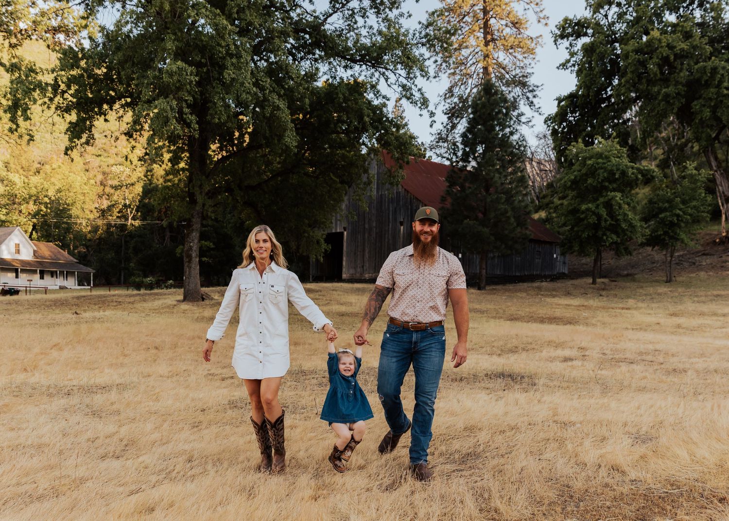 People walk together through a sunlit meadow with oak trees in the background.