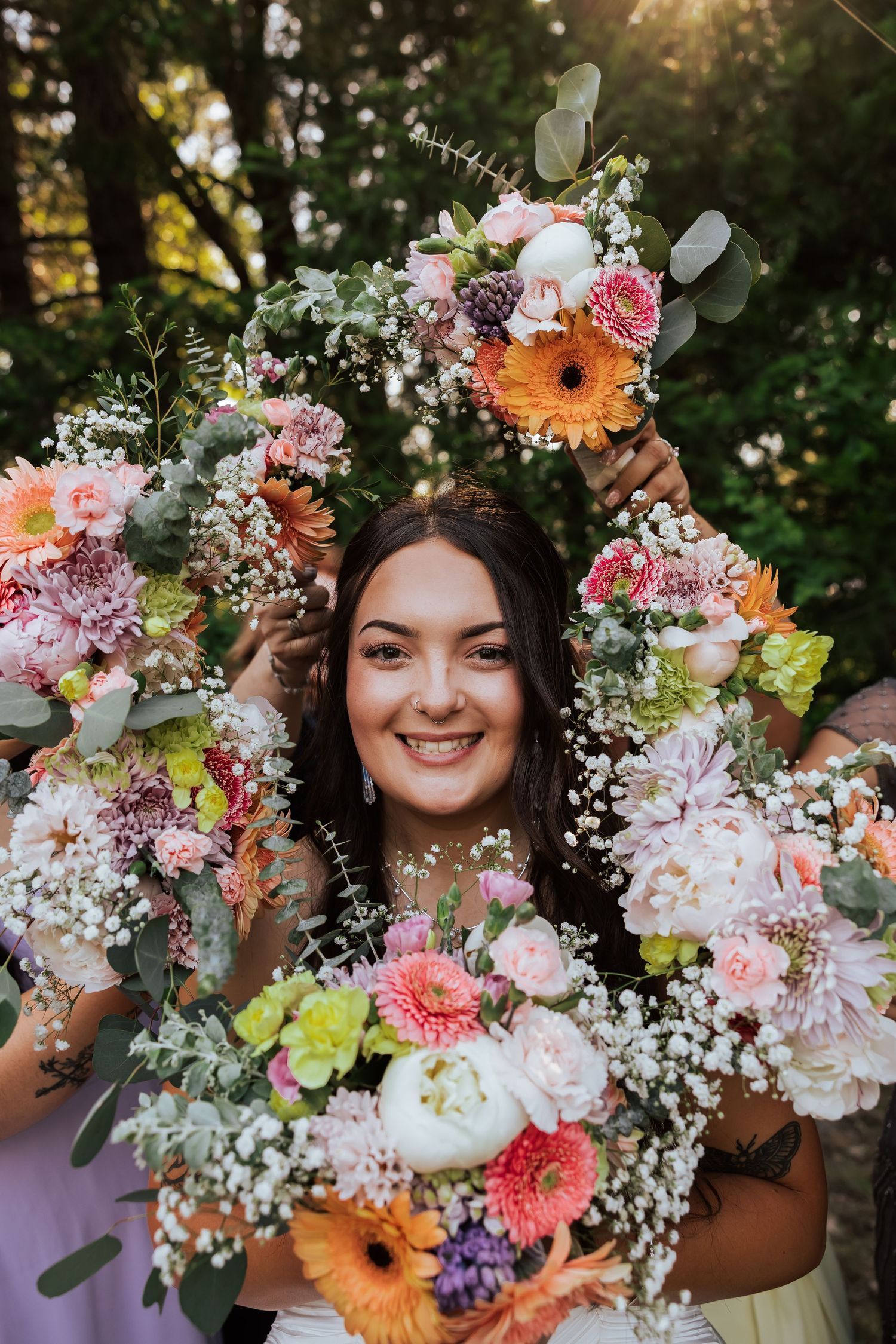 Smiling bride framed by colorful wedding bouquets featuring gerbera daisies, roses, and eucalyptus.