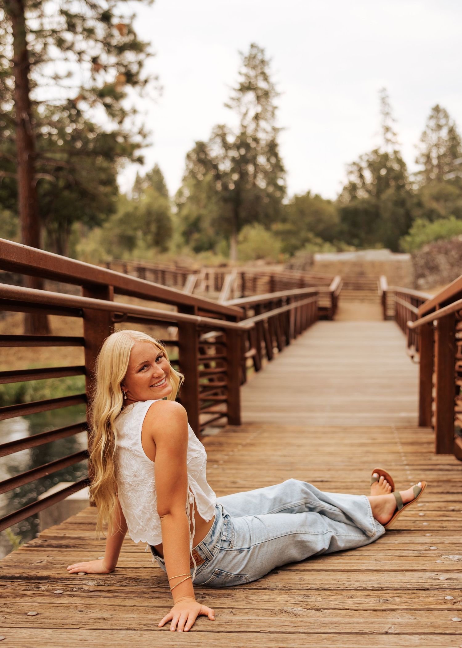 Outdoor portrait sitting on wooden bridge walkway surrounded by pine trees.