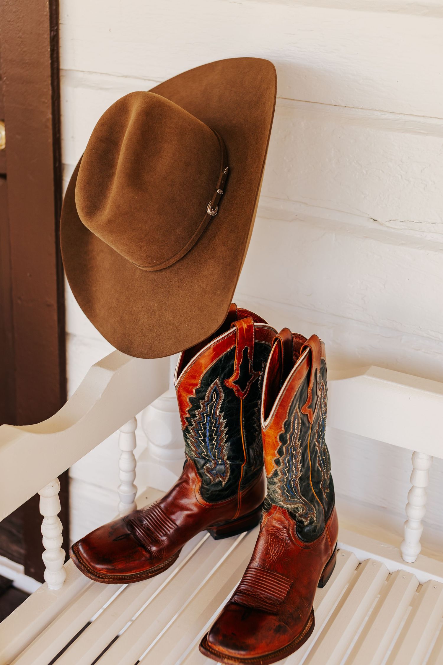 Brown cowboy hat and red leather boots displayed on a white wooden bench.