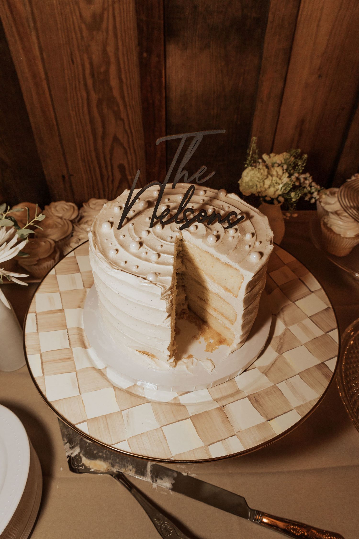 Partially eaten wedding cake on checkered plate with rustic wooden background.