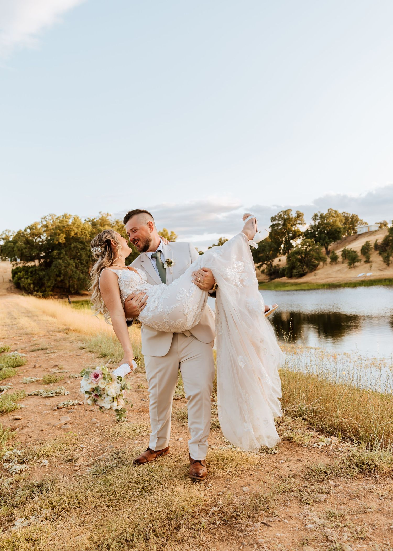 A groom dips his bride in a romantic pose during their lakeside wedding photo session.