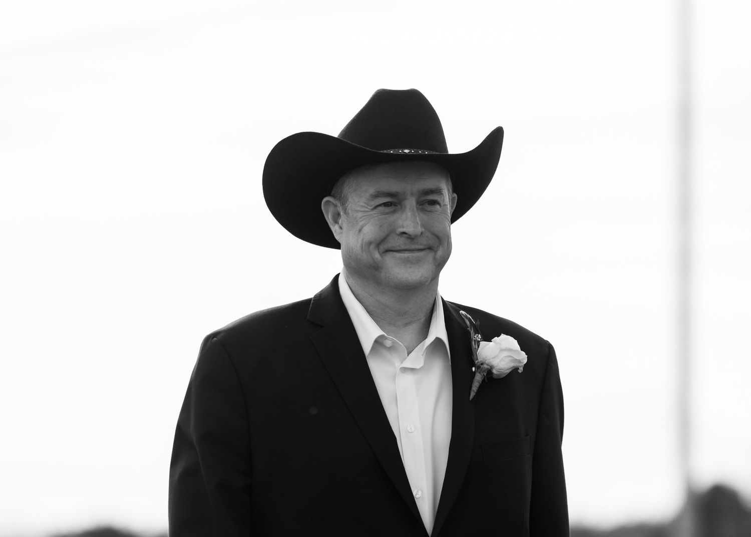 A row of groomsmen in black suits and cowboy hats stand against a white background.