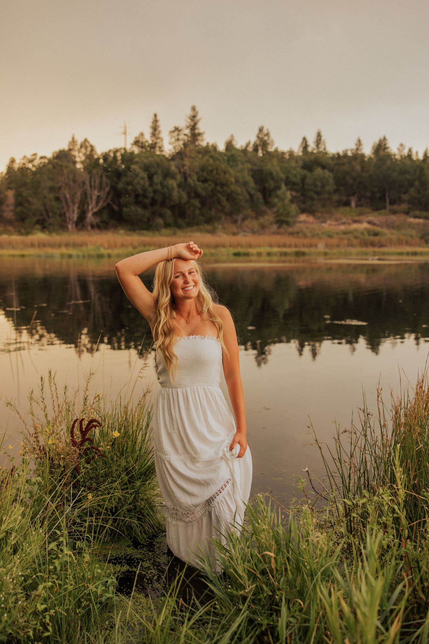Ethereal lakeside portrait with white dress against calm water and sunset sky.