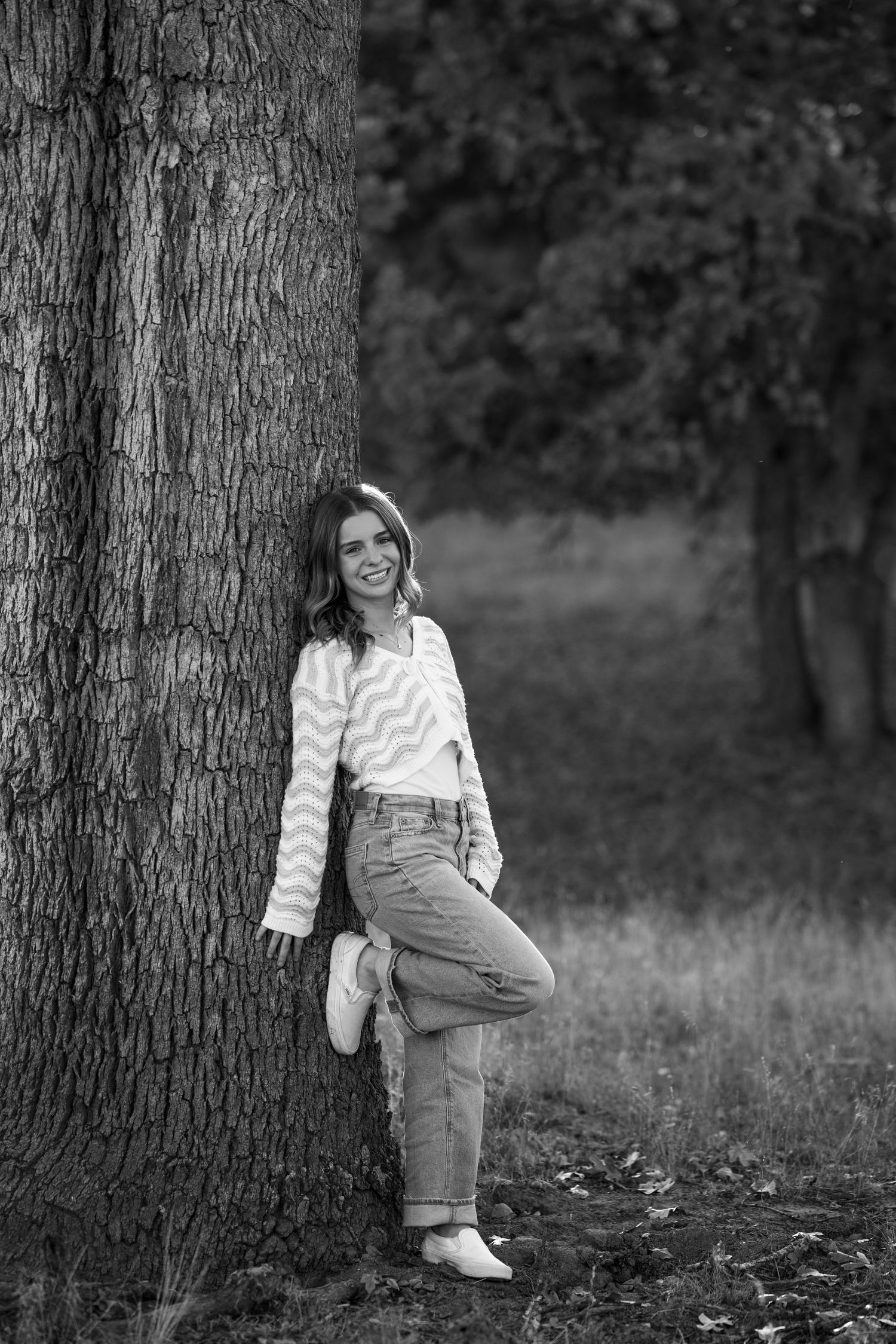 Black and white senior portrait with rustic tree backdrop and overalls.