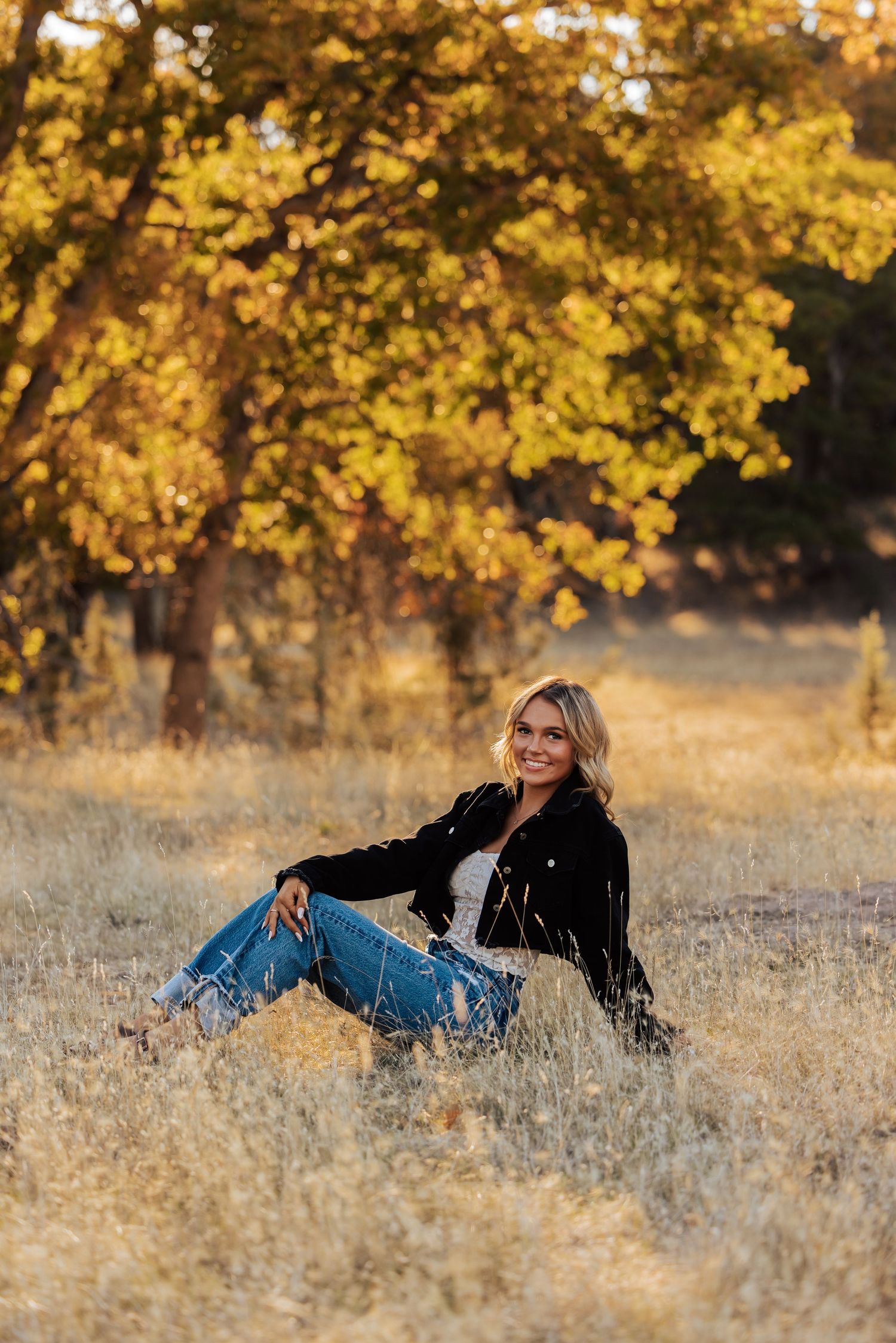 Relaxed outdoor portrait in tall grass with golden autumn trees creating a natural backdrop.