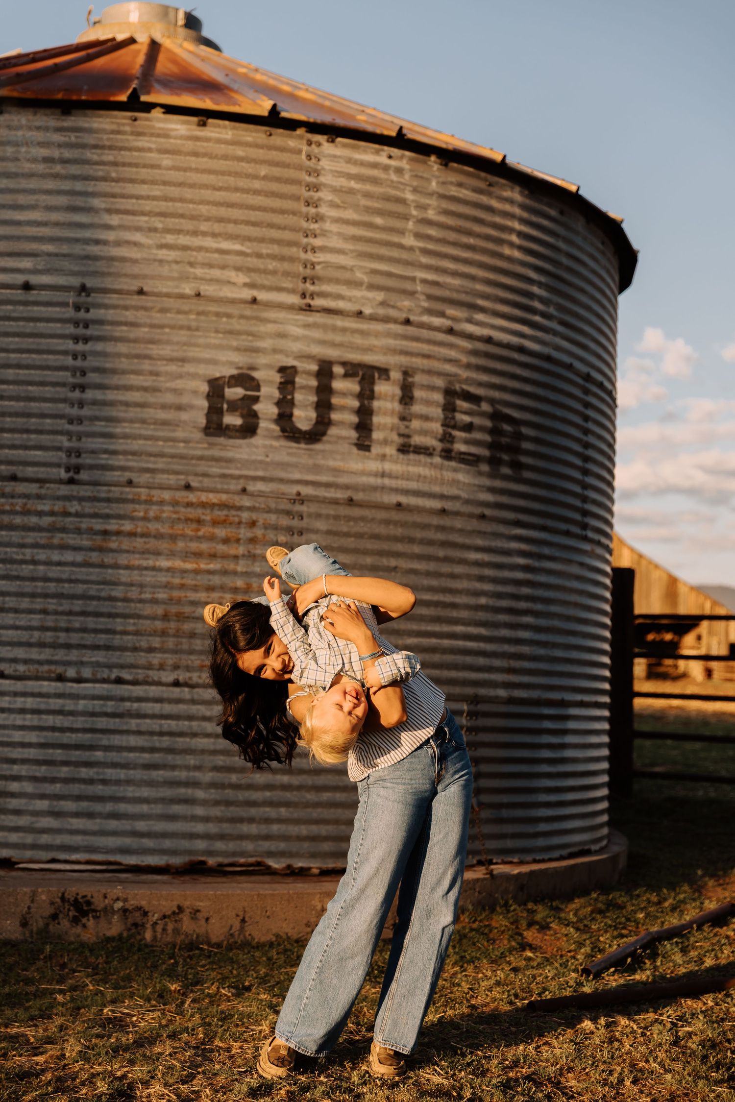 Couple poses playfully against metal grain silo at sunset.
